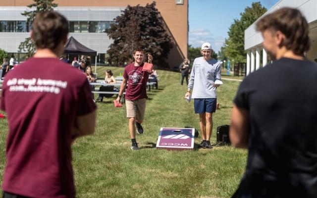 Four students playing cornhole outside on campus